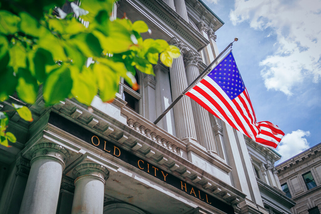 An old city all building with leaves blocking the frame and an american flag on the building flowing in the wind. 